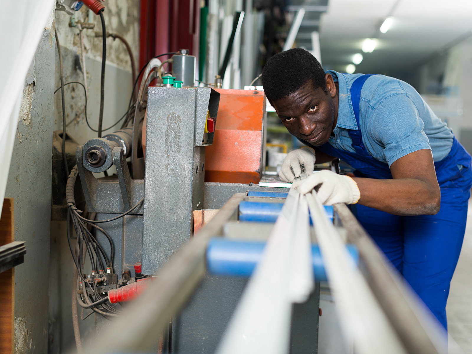 A man in a blue apron focuses on measuring a metal beam