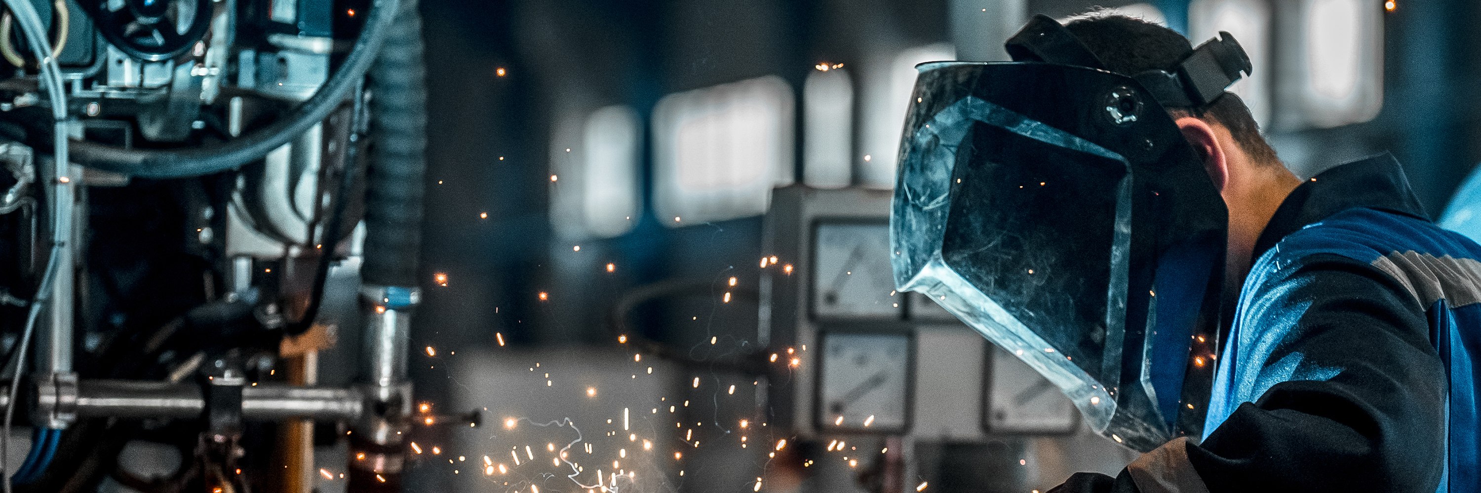 Welder wearing a blue protective face mask with sparks and machinery