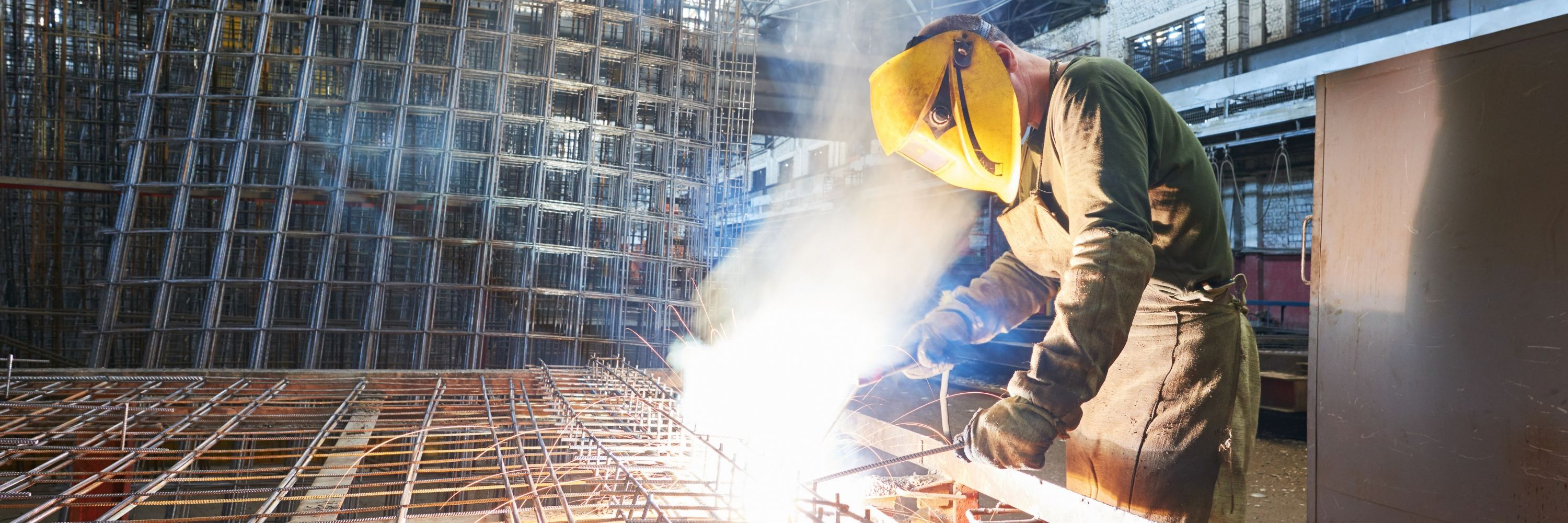 Welder in yellow protective mask using a heat tool to create a metal grid