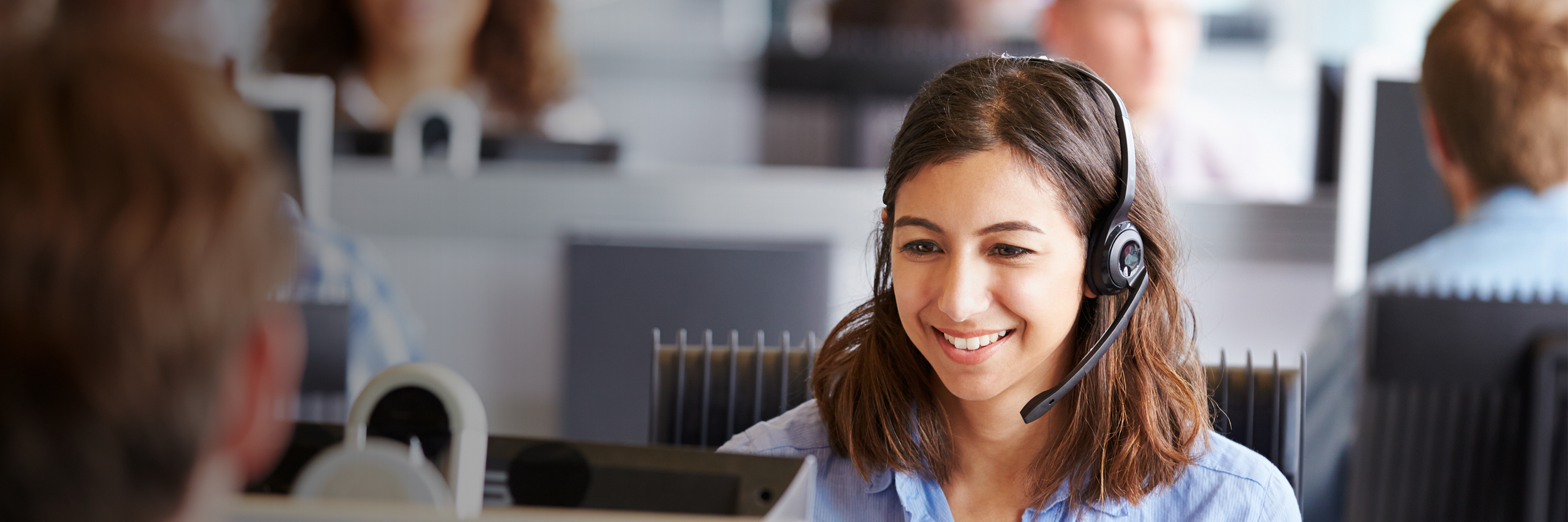 Woman looking at a computer wearing a headset and smiling