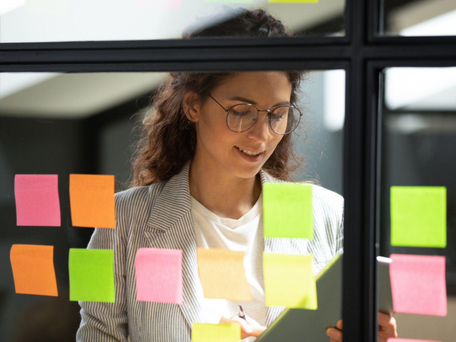 A woman looks over her organized sticky notes on a window as part of her project management