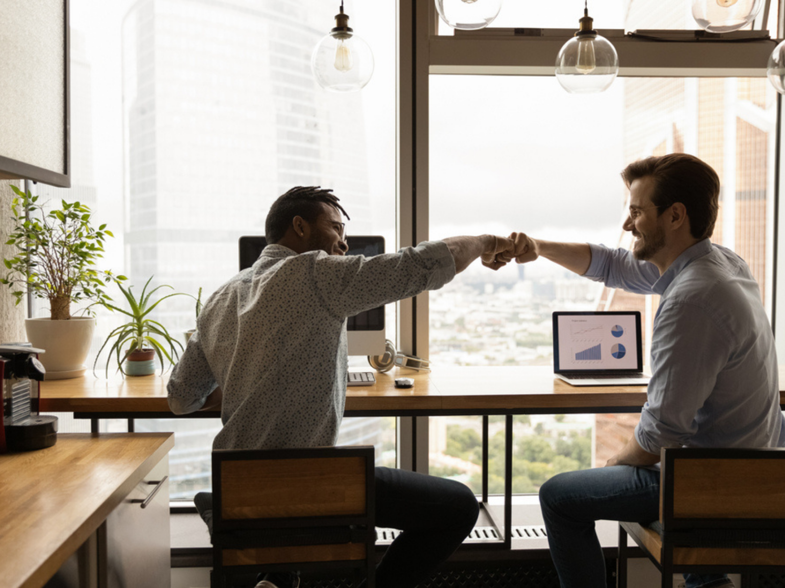 Two men fist bumping and celebrating their work success in a dim office setting