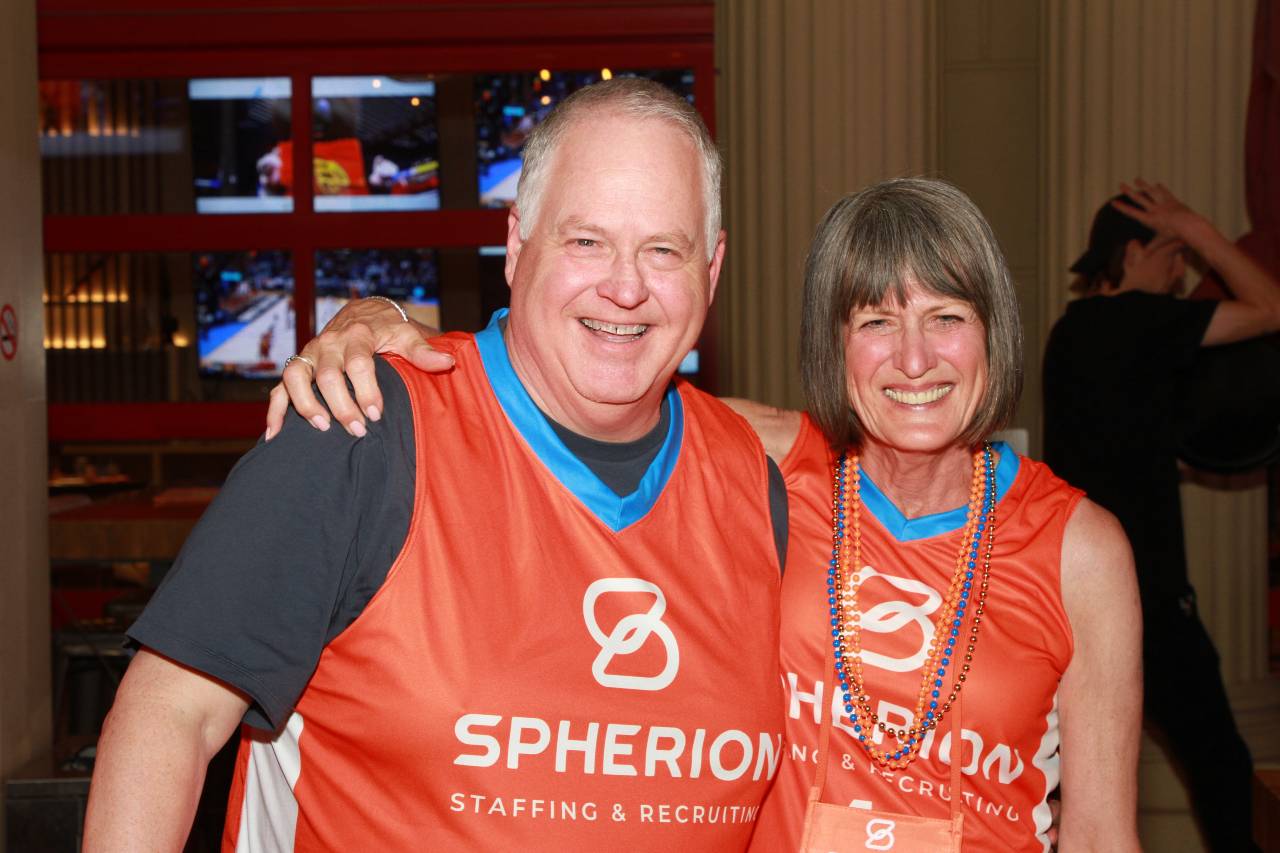 Two Spherion friends hugging and smiling for the camera wearing orange Spherion jerseys