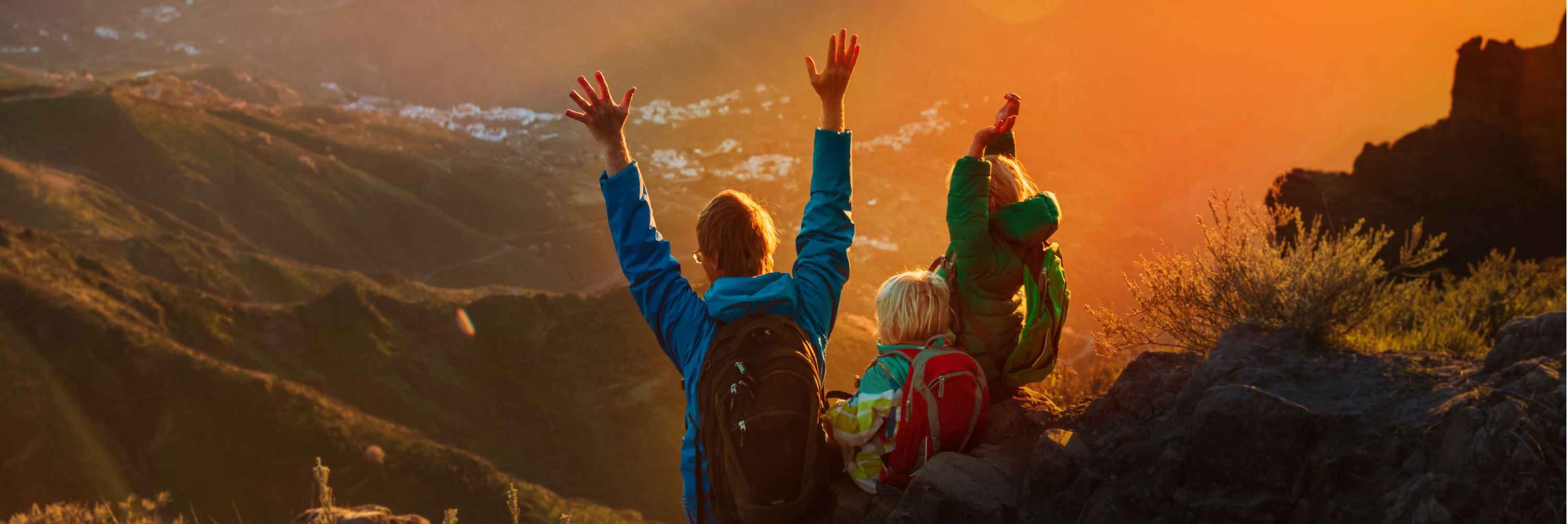 Family at the top of a mountain with arms raised at sunset