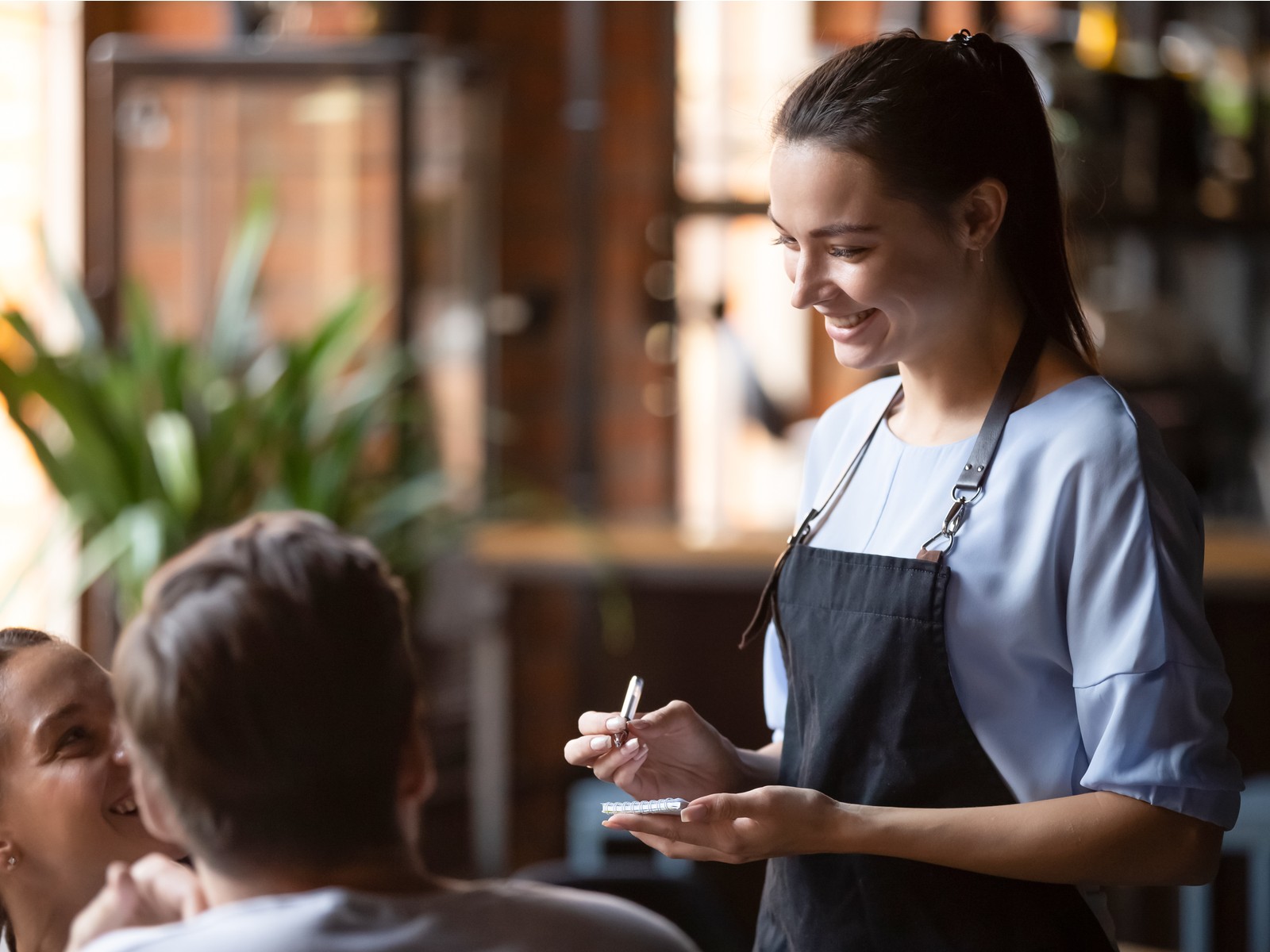 A female waitress smiles as she takes a customer's order