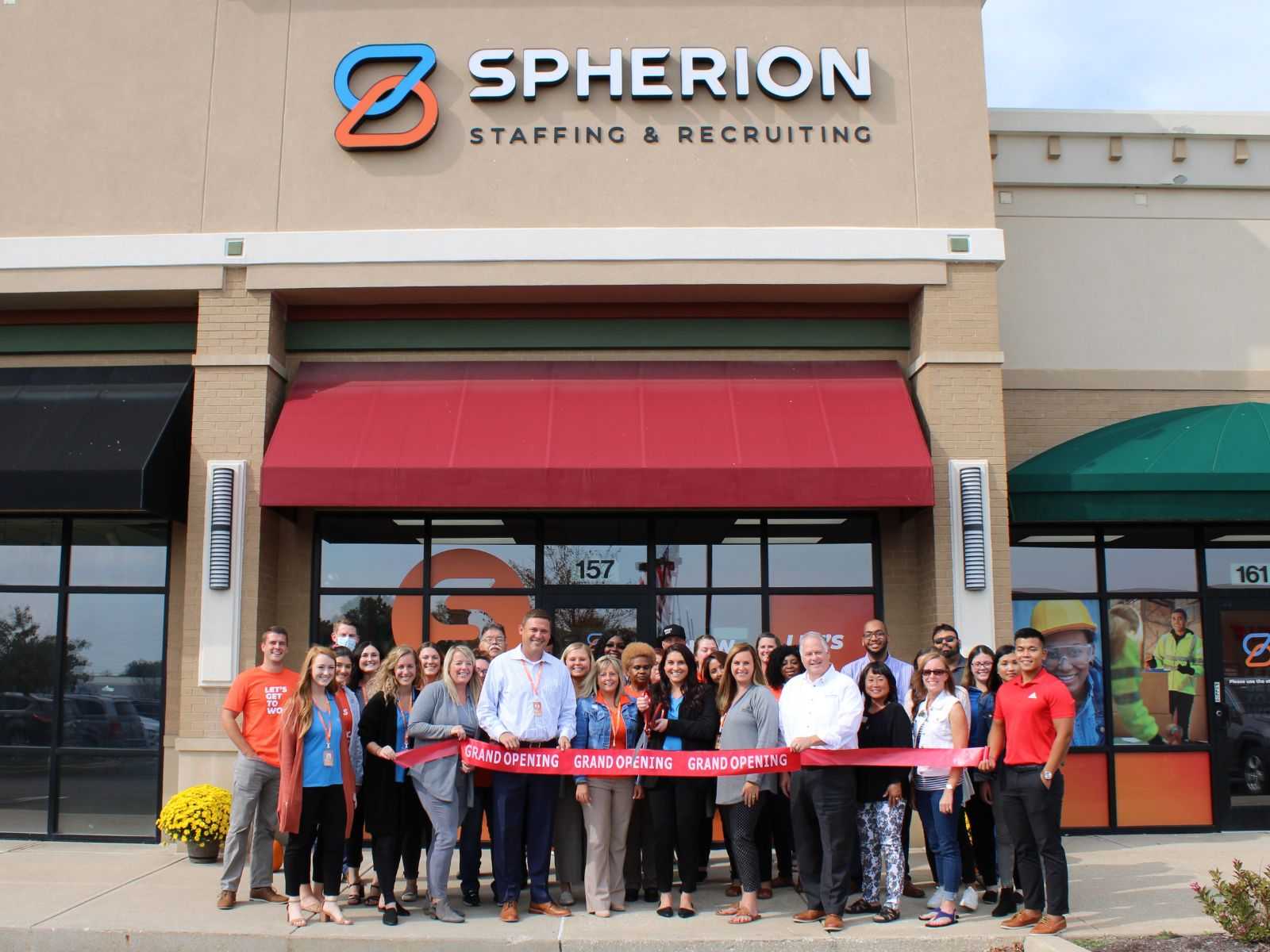 Grand opening of the Spherion Plainfield office. A group of Spherion employees poses with a grand opening ribbon in front of a Spherion storefront.