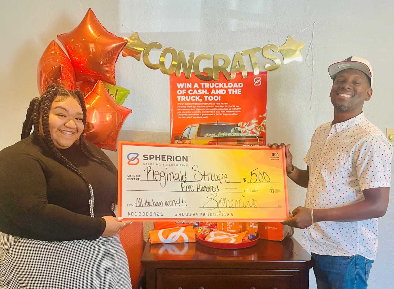 A Spherion female employee helps a Spherion Works Sweepstakes winner hold up a giant $500 check