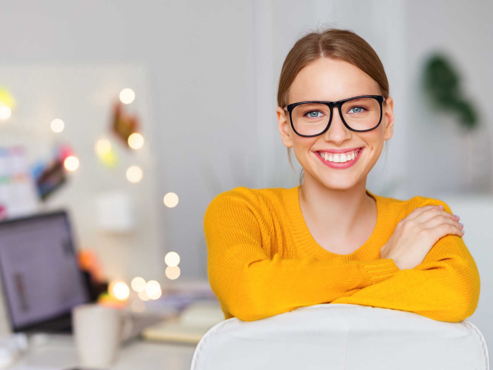 Woman in orange sweater wearing glasses smiling at camera