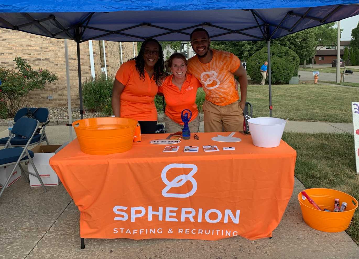 Three people gathered at an orange Spherion table under a blue tent outside