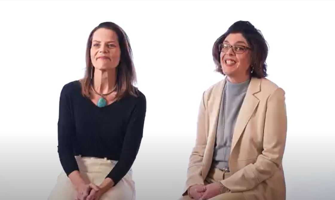 Two women sitting on stools against a white background