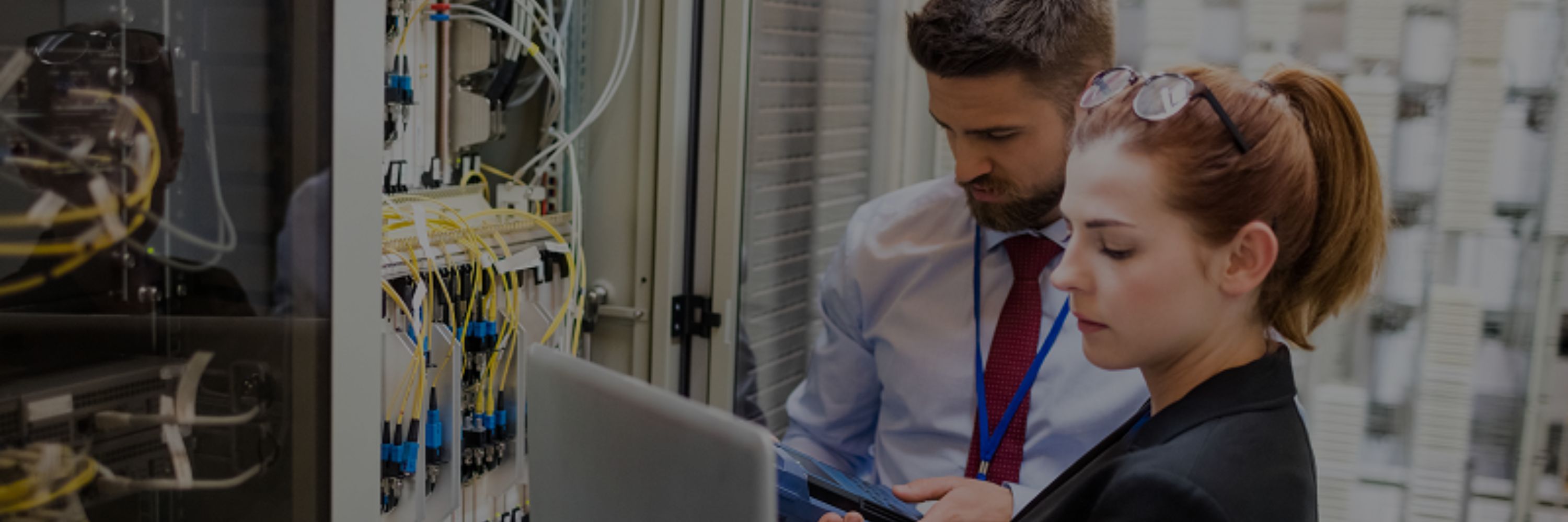 Woman and man working in a server room looking at a laptop