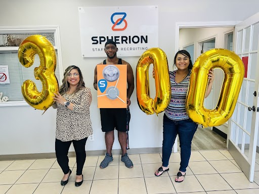 Three people holding gold balloons that spell out the number 300, in an office with the Spherion logo in the background