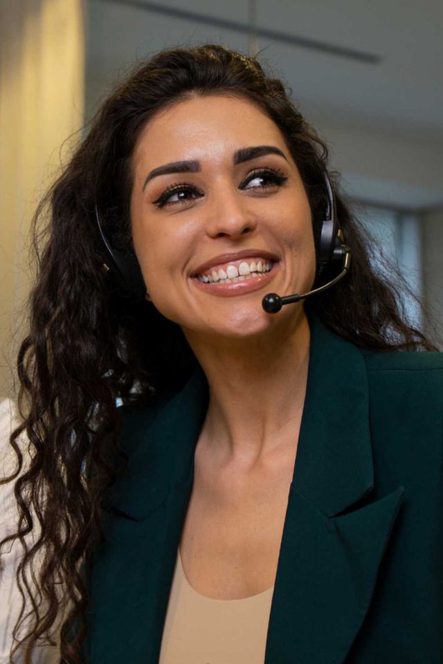 A dark-haired woman wearing a headset and smiling