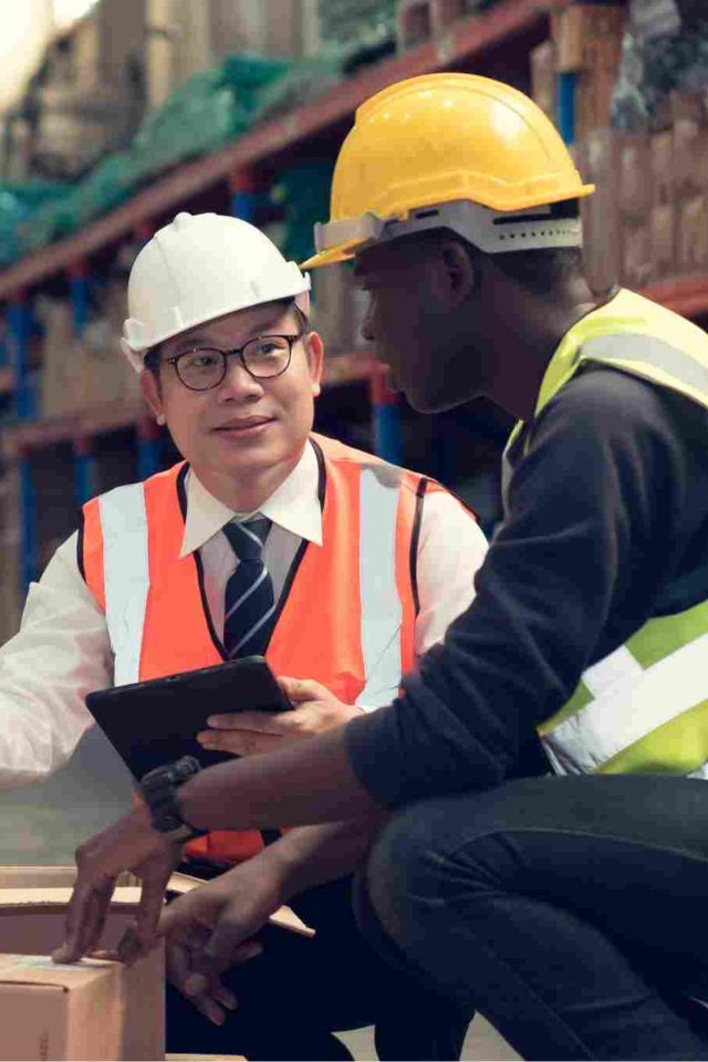 Two men in hard hats and safety vests in a warehouse setting