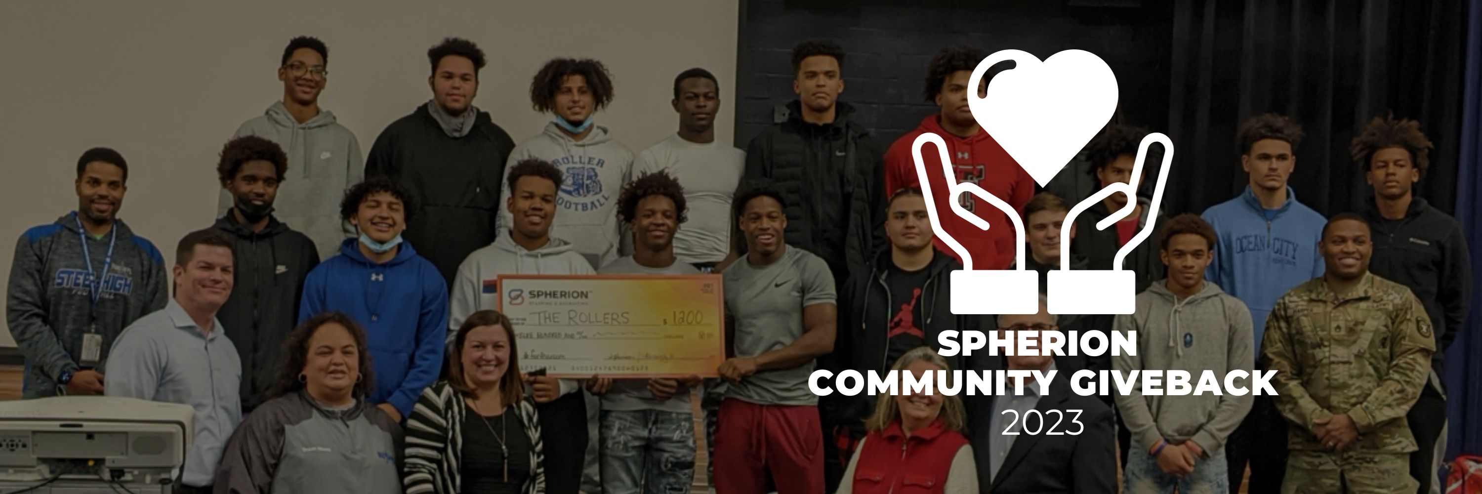 A group of young people smiling and holding a check for $1200. A white logo features two hands holdinga heart and the text, Spherion Community Giveback 2023