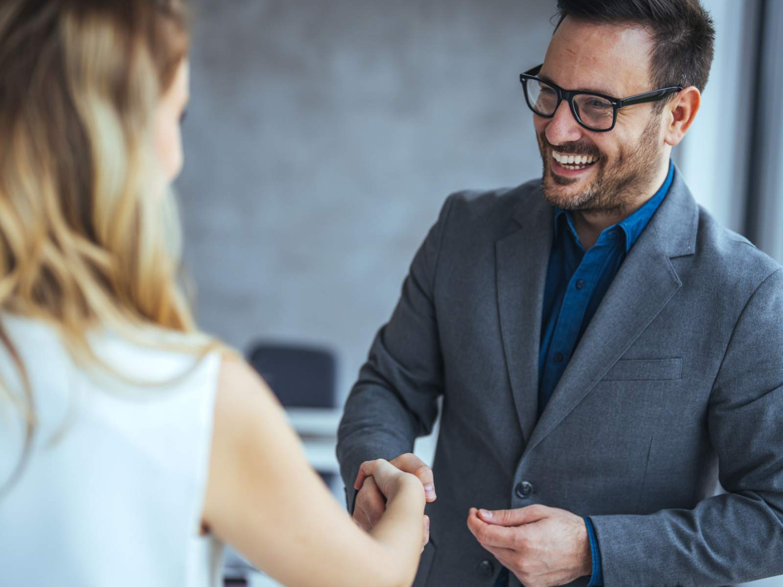 Smiling man in a gray suit and blue shirt shaking hands with a woman in a white shirt