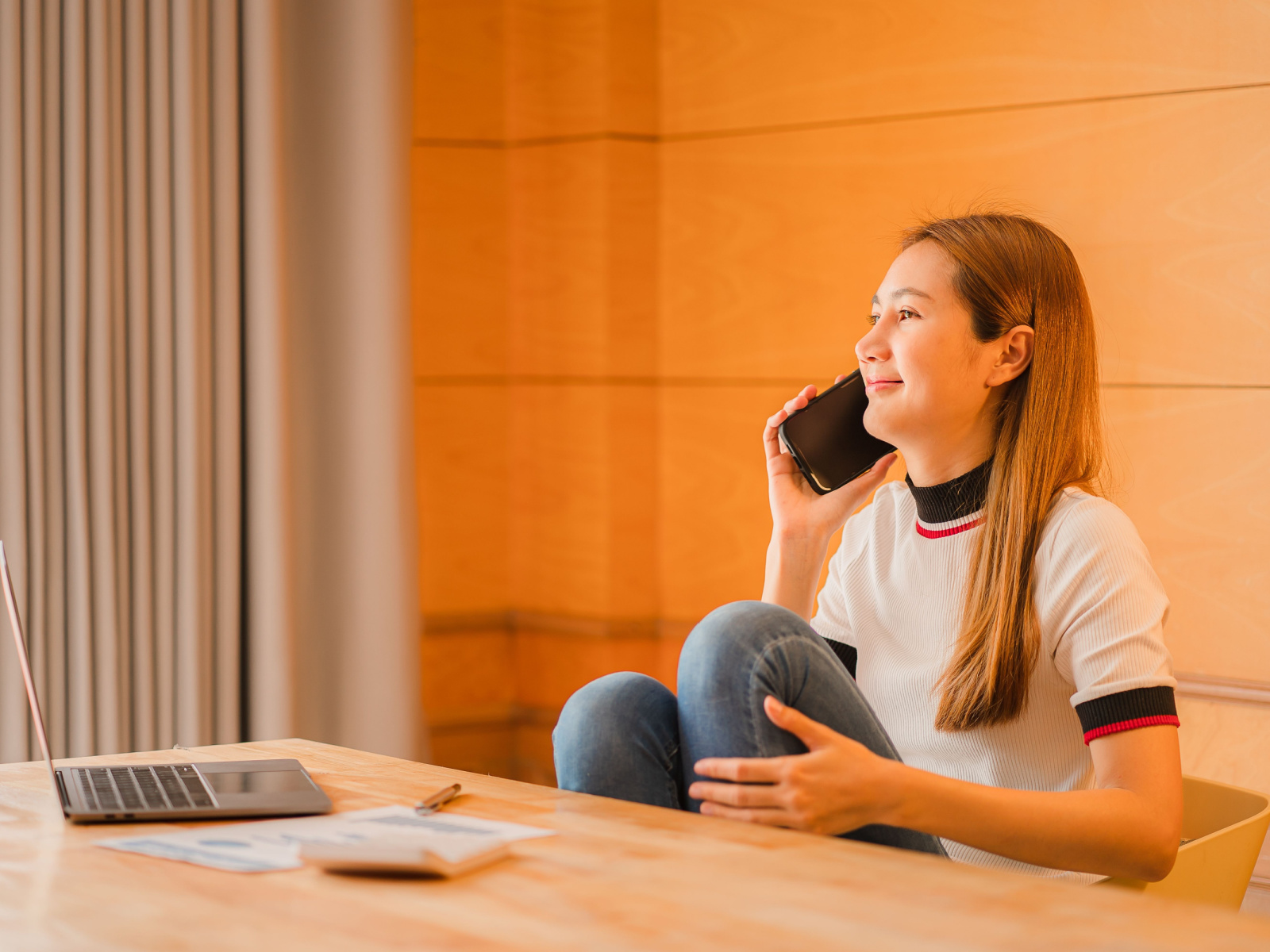 Young Asian businesswoman talking on the phone on her laptop sitting at her desk at home