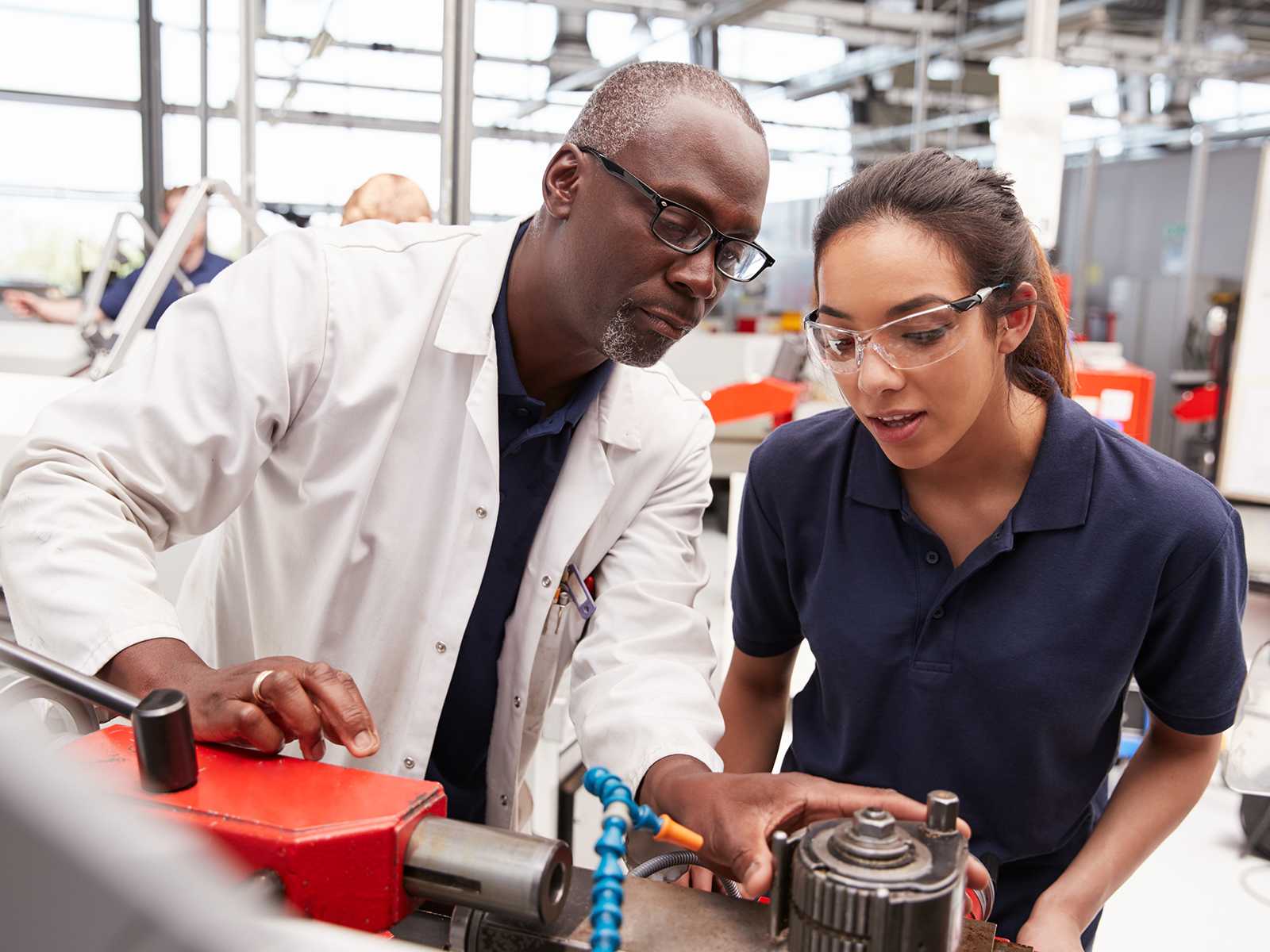 Black man in a lab coat next to a Hispanic woman in a blue shirt inspecting a piece of equipment