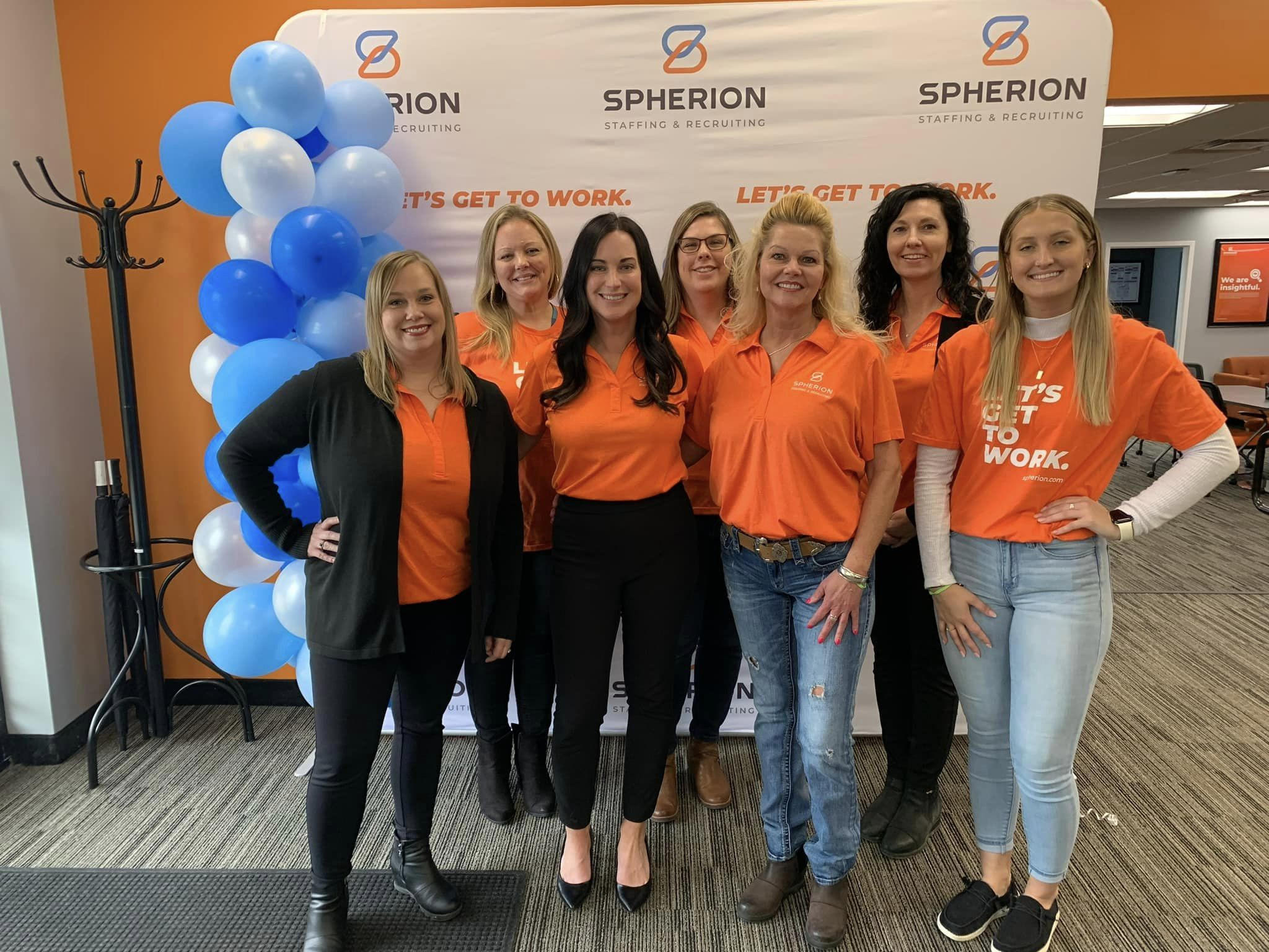 A group of women in orange shirts smiling and posing in an office setting