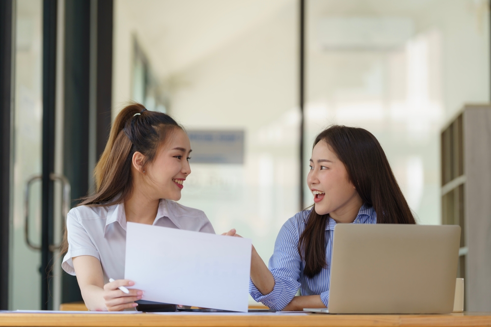 Two Asian businesswomen discuss new startup project idea presentation and analyze planning and financial statistics and investment market at the office