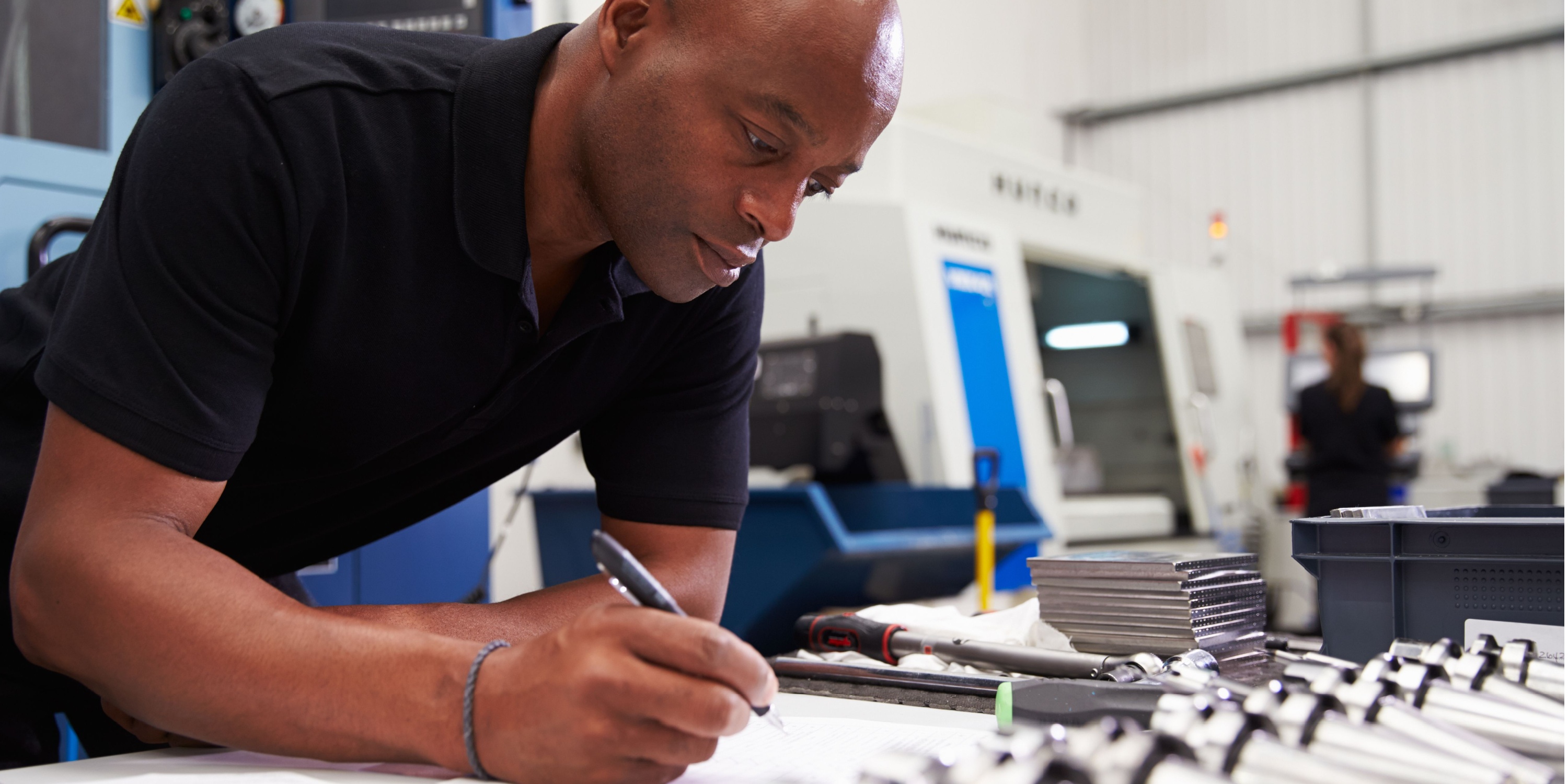African-American male inspecting blueprints for a CNC machine