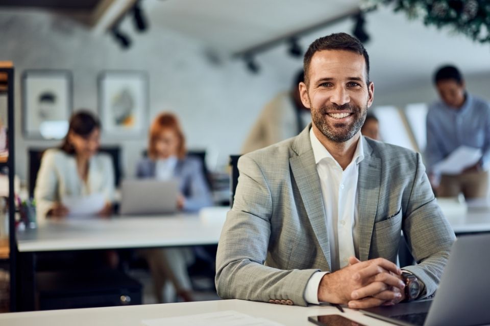 A young male in a suit smiling and sitting at a desk