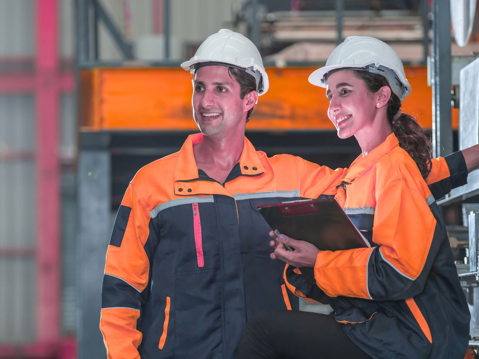 A man and woman in orange safety suits in a manufacturing plant