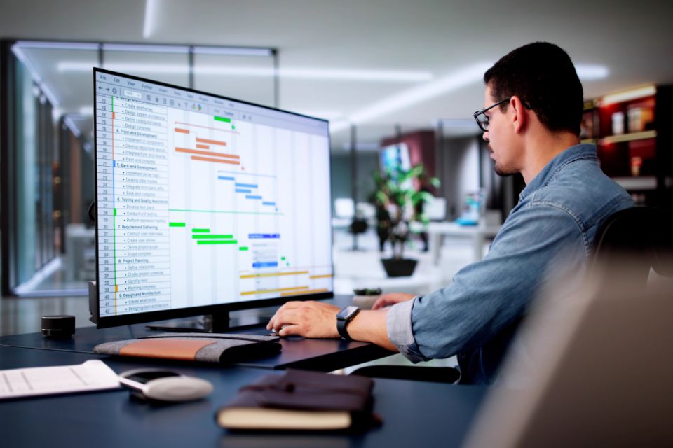 Man sitting a desktop computer showing a kanban board