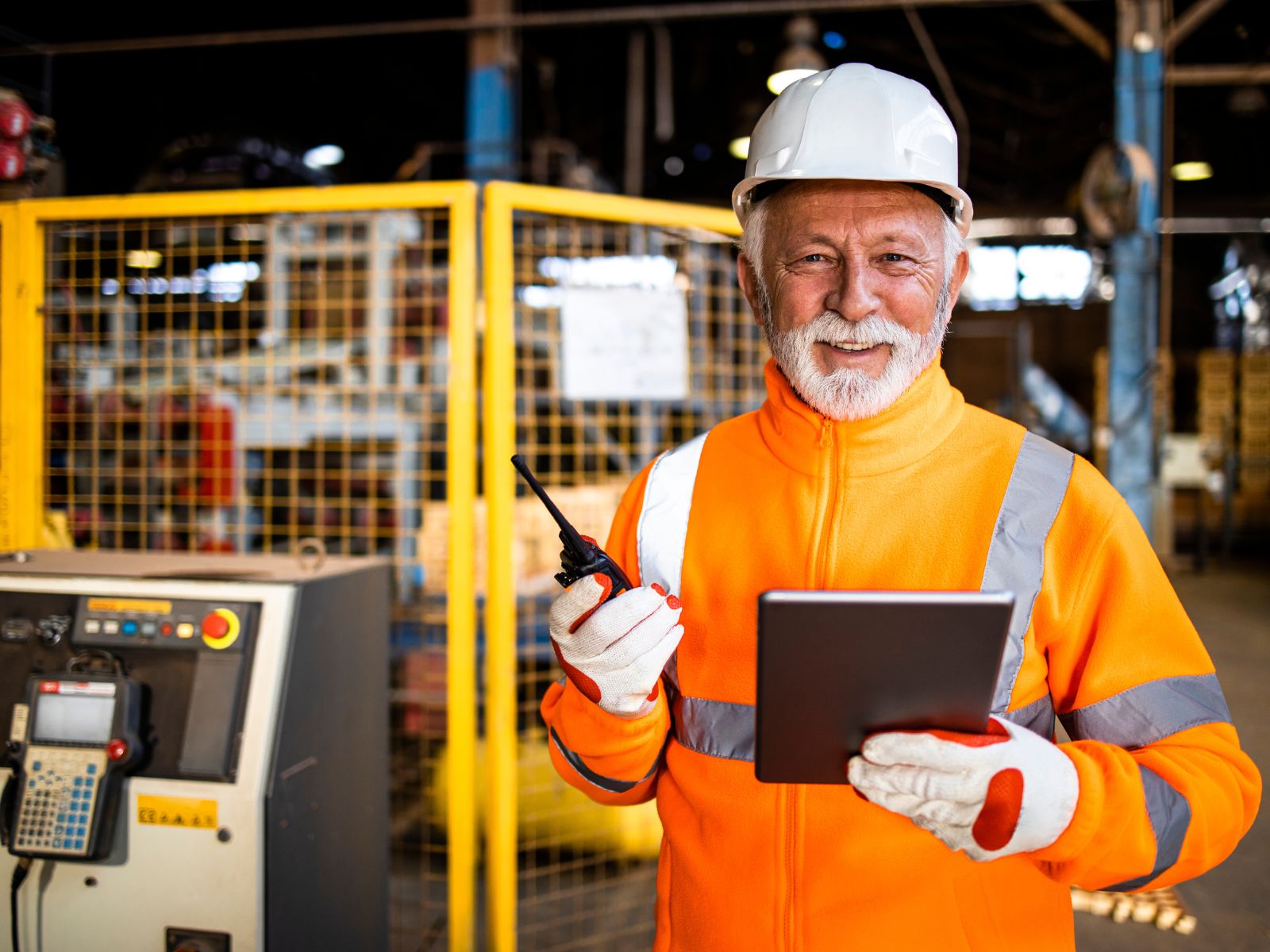 Older man in orange safety vest smiling in a factory setting