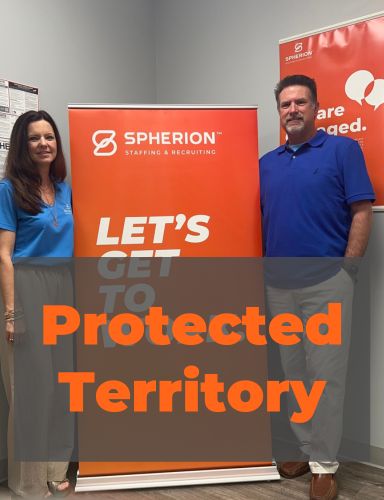 A woman and man standing by an orange banner that reads, Let's Get to Work
