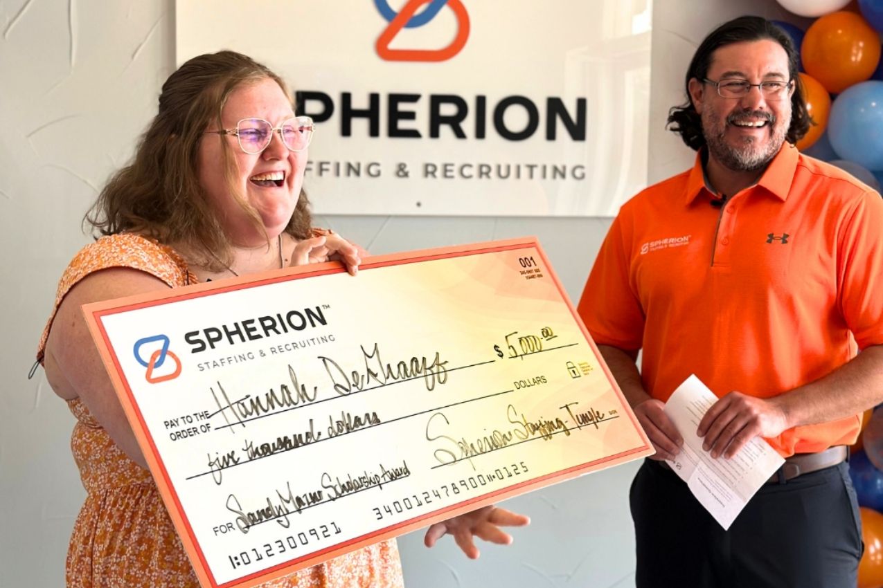 Photo of a young woman smiling and holding a big check next to a man in an orange shirt
