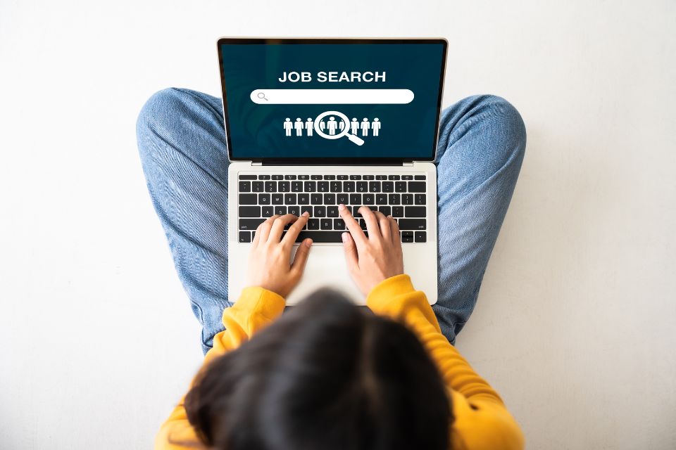 Birds-eye view of a young woman sitting on the floor with a laptop doing a job search online