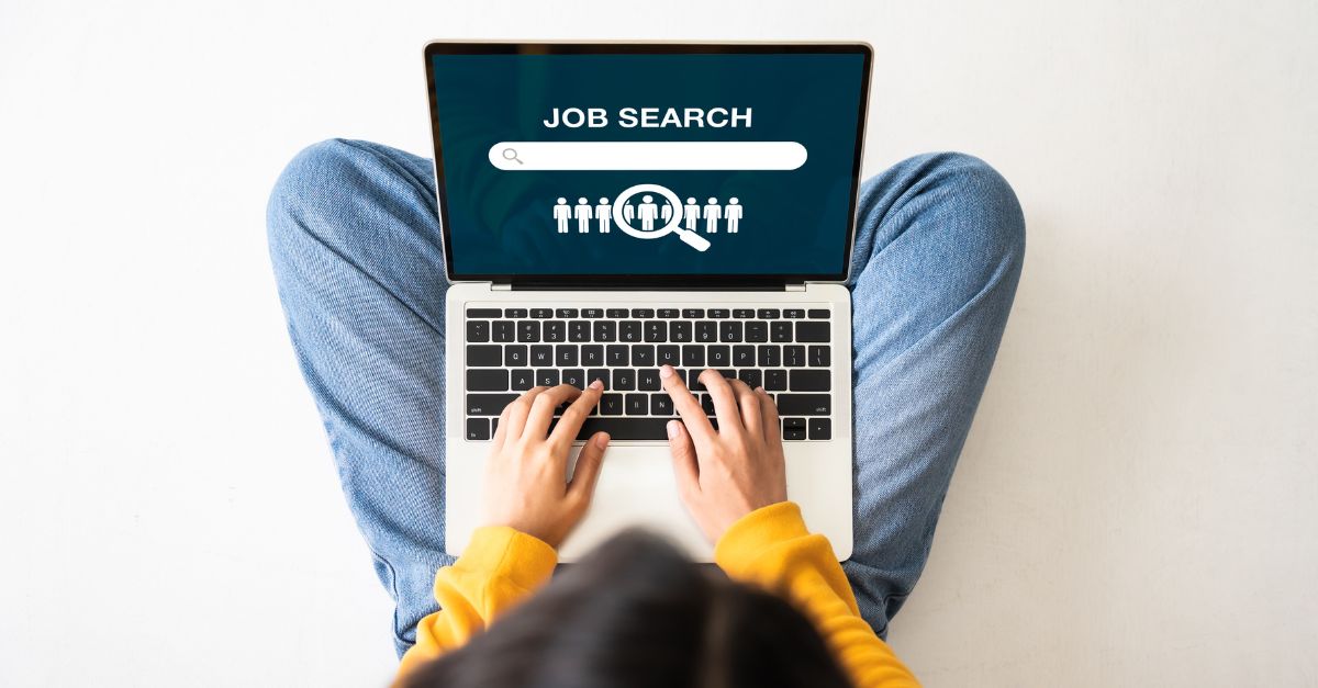Birds-eye view of a young woman sitting on the floor with a laptop doing a job search online