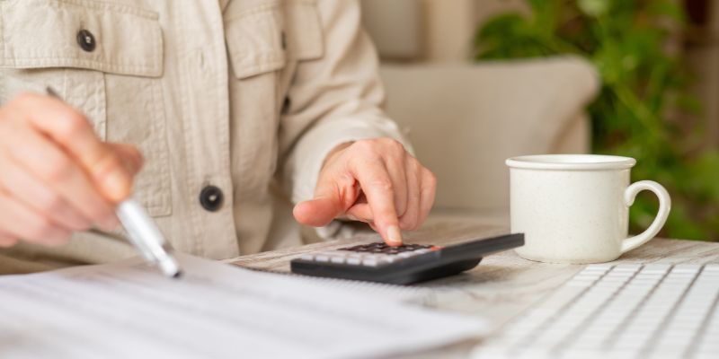 Middle-aged woman using calculator and pen at home office desk