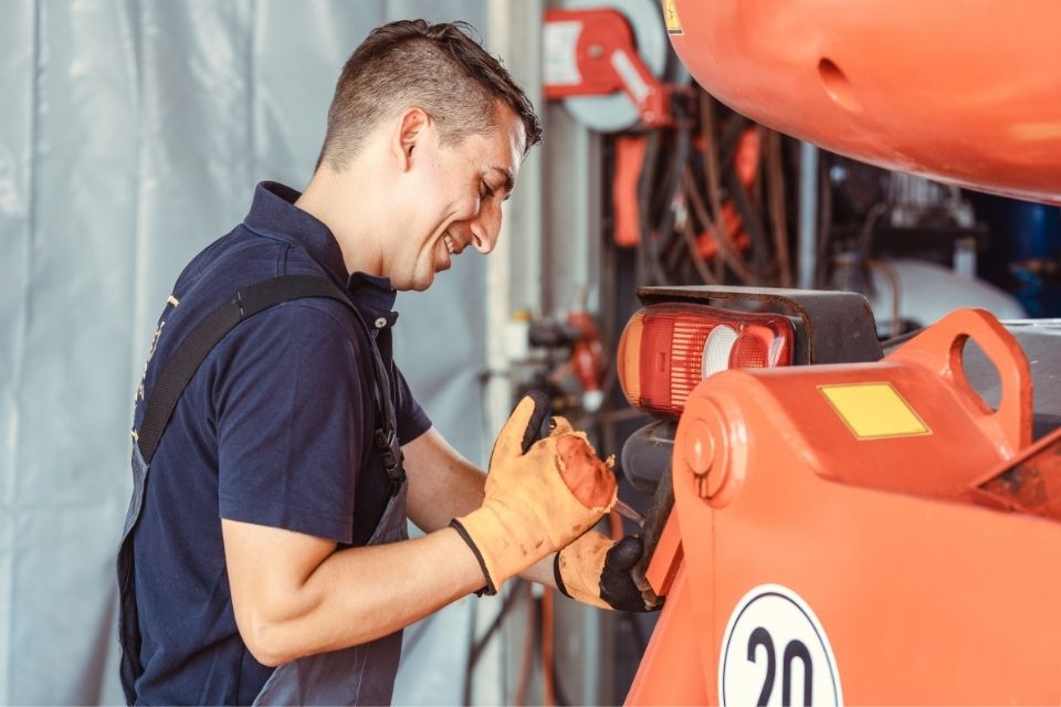 A male mechanic works on an orange engine