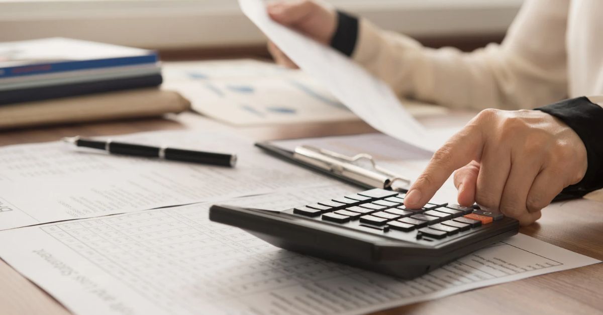 Close-up photo of a person's hands holding budget documents and using a calculator.