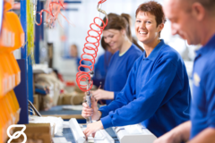 A woman in a blue suit smiles as she works on a product assembly line.