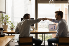 Two men fist bumping and celebrating their work success in a dim office setting