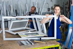 A woman, foreground, and a man, background, assemble white metal frames at work.