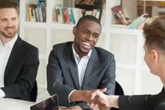 Black man in suit smiling and shaking hands with white man