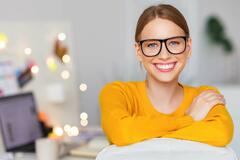 Woman in orange sweater wearing glasses smiling at camera