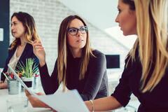 3 professional women sitting at a table holding papers and talking