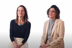 Two women sitting on stools against a white background