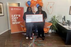 Two women holding a giant scholarship check in front of an orange banner that reads Let's Get to Work