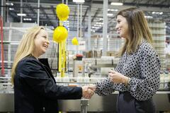 Two women shaking hands and smiling in a factory setting