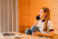 Young Asian businesswoman talking on the phone on her laptop sitting at her desk at home