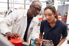 Black man in a lab coat next to a Hispanic woman in a blue shirt inspecting a piece of equipment