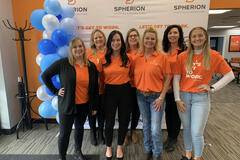 A group of women in orange shirts smiling and posing in an office setting