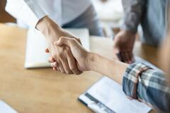Overhead view of two people shaking hands over a table with documents on it
