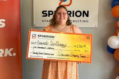 A girl holding a giant orange check standing by an orange banner and a Spherion logo sign